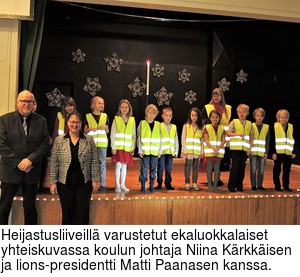 Heijastusliiveill varustetut ekaluokkalaiset yhteiskuvassa koulun johtaja Niina Krkkisen ja lions-presidentti Matti Paanasen kanssa.