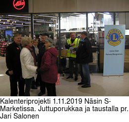 Kalenteriprojekti 1.11.2019 Nsin S- Marketissa. Juttuporukkaa ja taustalla pr. Jari Salonen