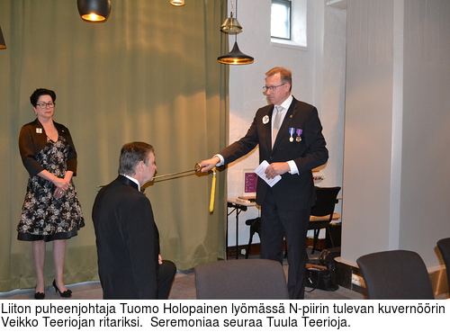 Liiton puheenjohtaja Tuomo Holopainen lymss N-piirin tulevan kuvernrin Veikko Teeriojan ritariksi.  Seremoniaa seuraa Tuula Teerioja.